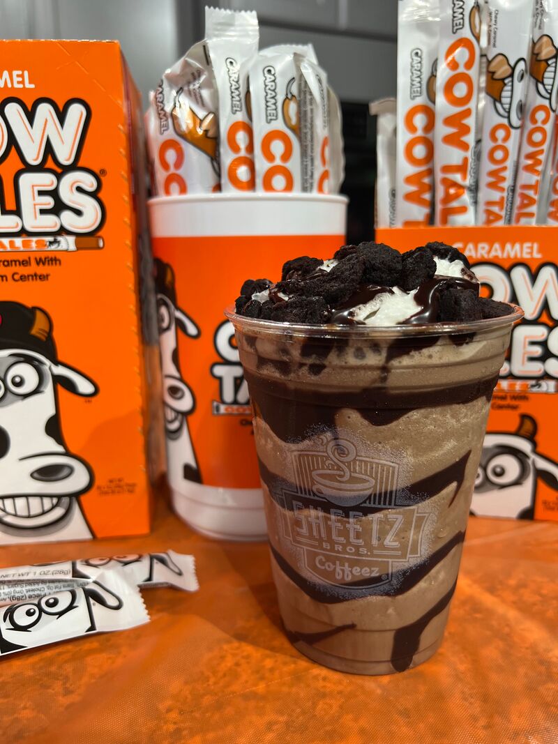 Caramel Brownie Cow Tales milkshake with whipped cream and crumbled brownies on top, layered with chocolate syrup throughout.