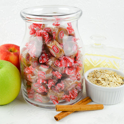 Jar filled of Caramel Creams with two apples, two cinnamon sticks, and a bowl of oatmeal.
