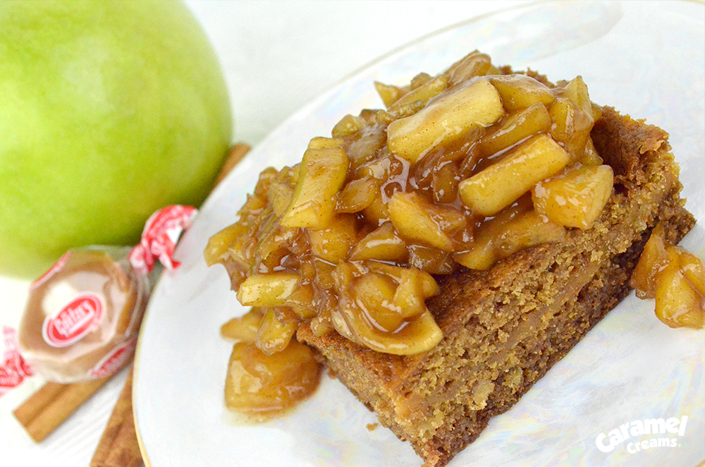 a portion of Caramel Apple Cookie Bars on a plate with a caramel cream, apple, and cinnamon sticks