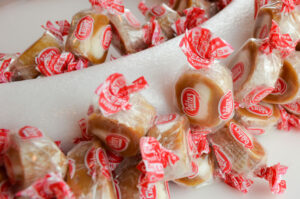 Close-up of a white foam wreath being decorated with Goetze’s Caramel Creams® candies, each wrapped in red and white packaging and secured around the surface.